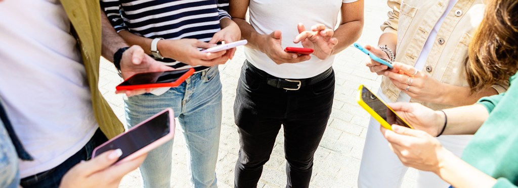 A group of young people using mobile phones while standing outside